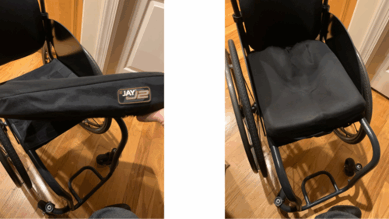 Two photos of a black wheelchair: the left image shows a hand lifting a black JAY J2 seat cushion designed for preventing pressure sores, and the right image shows the cushion on the wheelchair seat. The wheelchair is on a wooden floor.