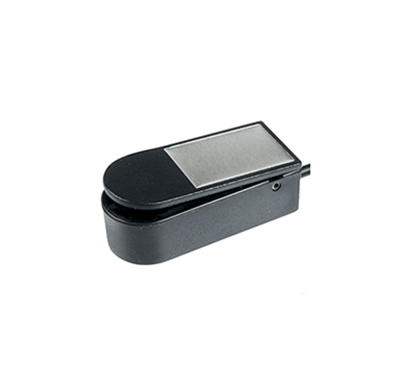 A black foot pedal switch with a rectangular silver metal top, placed on a white background. The pedal has a rounded front, an attached wire on one side, and is commonly used for assistive technology applications.