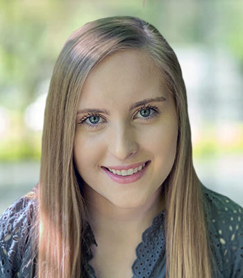 A young woman with long, straight blonde hair, blue eyes, and a friendly smile, wearing a grey lace top, sits in front of a softly blurred green outdoor background—perfect for promoting personalized speech solutions.